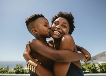 Boy kissing on cheeks of her mother. Cute boy hugging his smiling mother and kissing in her face.